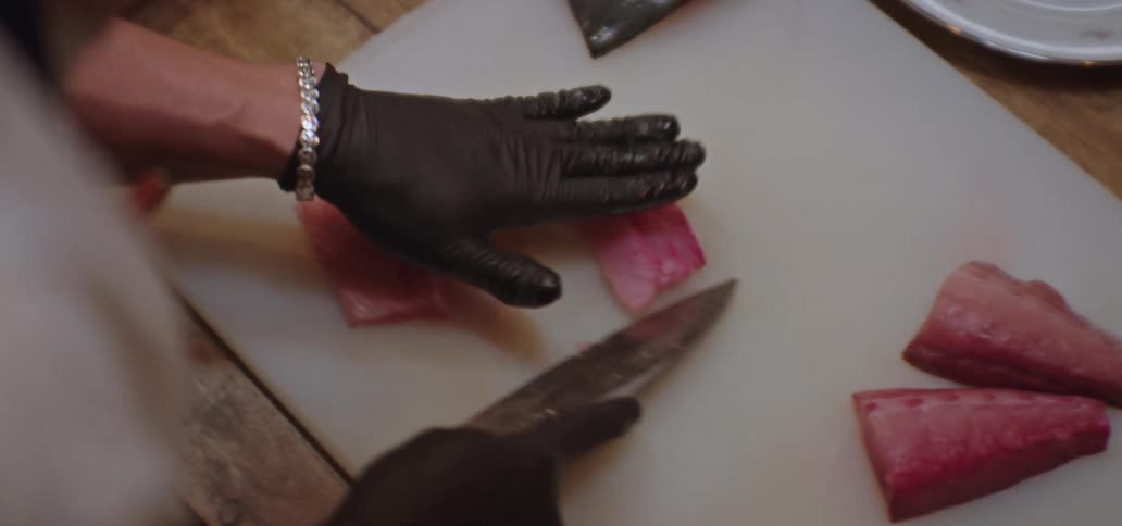 A man carefully cuts fish into slices and places on plates with sauce