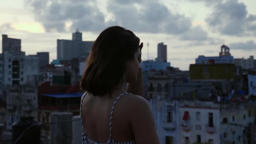 A woman stands on a rooftop overlooking a city