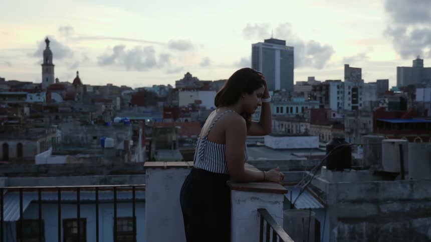 A woman stand on a patio overlooking city rooftops