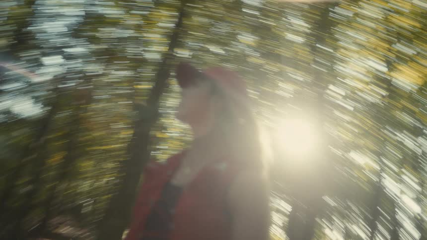 Blurred person wearing a red cap walking through a sunlit forest