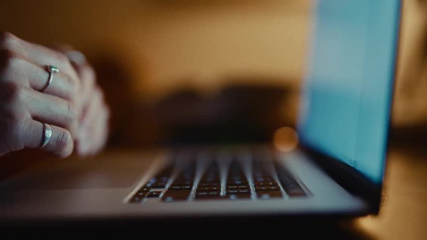 Hands wearing silver rings are illuminated by the blue glow of a laptop screen