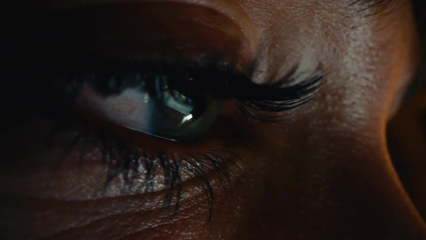 The eye of a person with long eyelashes looking at something that is reflecting a bright image in their eyes