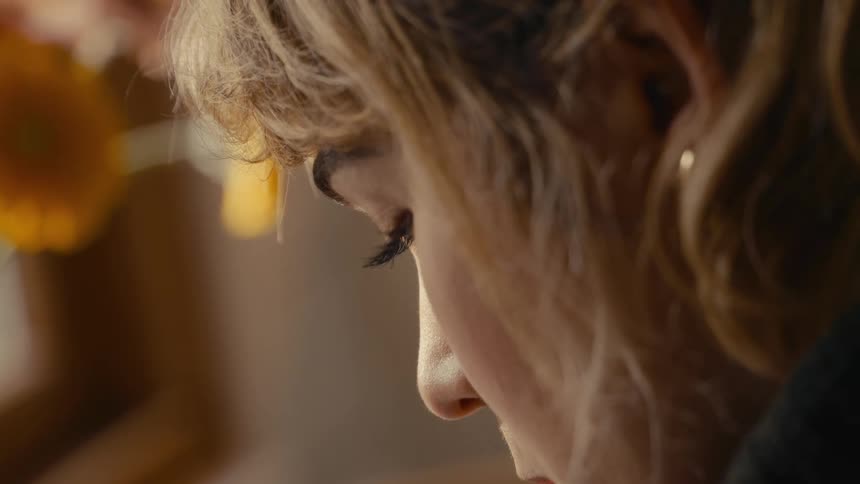 An extreme closeup captures the soft profile of a woman concentrating her gaze directed downward as warm intense focus in a softly lit room