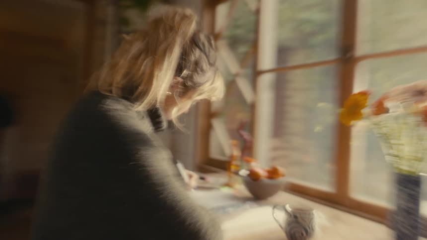 A young woman sitting at a desk by the window writing on paper with a pen indoors at midday