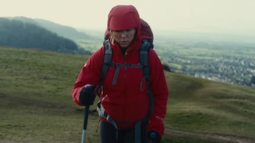 Young adult woman wearing a red hood and carrying a backpack hiking outdoors during day time