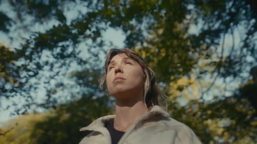 Young woman standing in the forest looking up as sunlight shines on her face