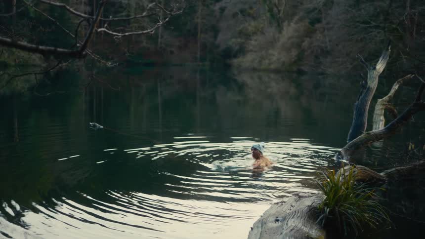 Young woman looks around as she swims in a river in the forest
