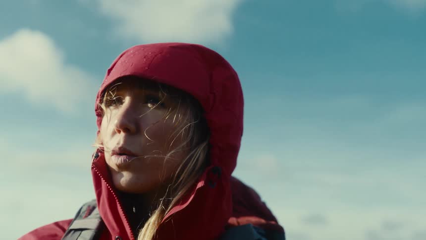 Woman in red jacket faces the horizon under a partly cloudy and windy sky