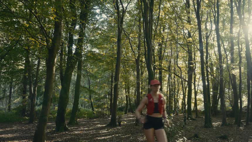 A woman wearing red sportswear is running in an ancient forest with thin trees