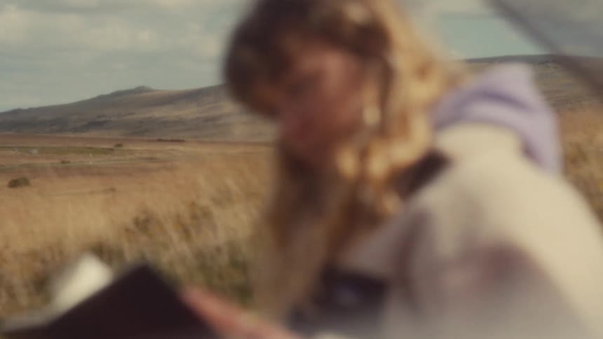 Blurred person holding a notebook in an open field with hills in the background