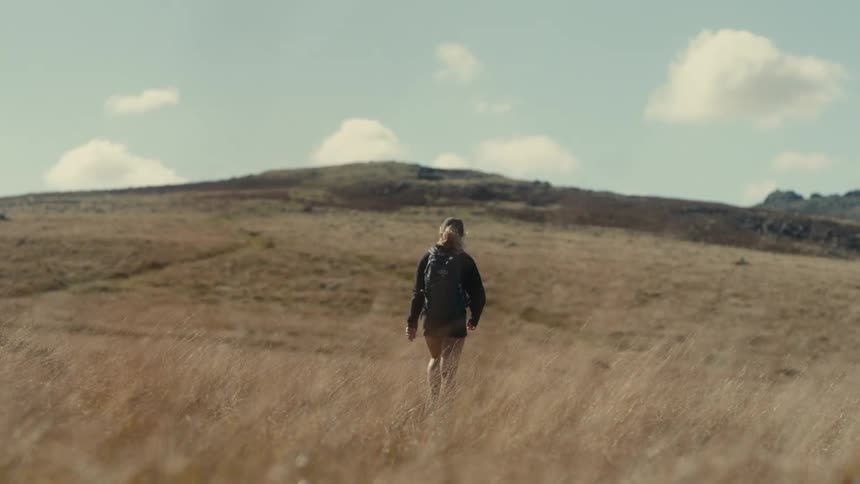 Female person wearing a baseball cap and carrying a backpack walking outdoors towards a slope