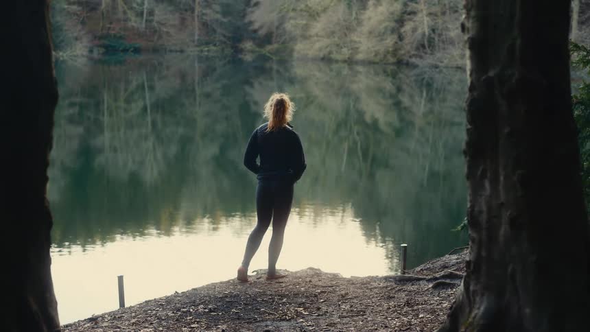 A woman stands at the edge of a lake