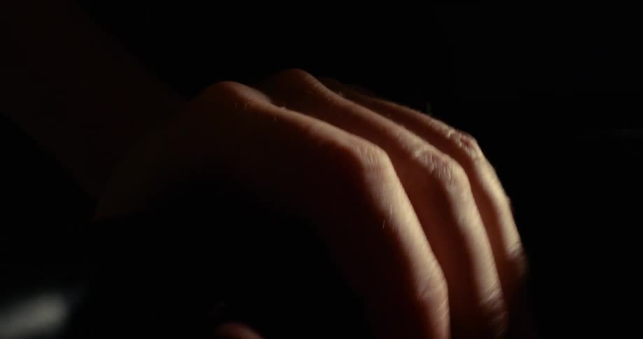 Male hand gripping against a bar on a dark room indoors