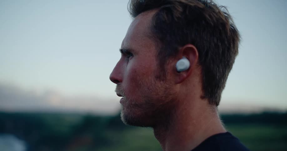 The man listens to his earbuds by the water