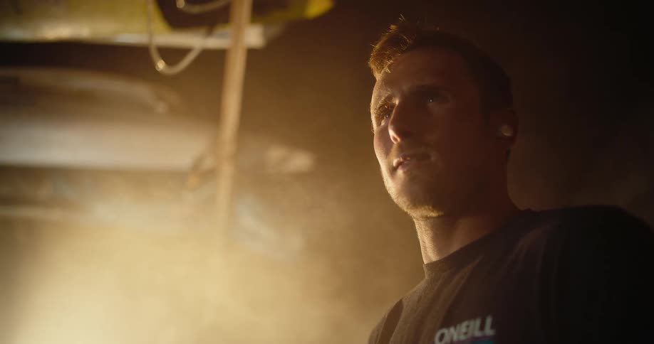 The image shows the face of a man standing indoors wearing white headphones with some smoke billowing behind him