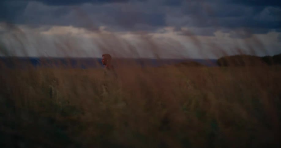 Man running through tall vegetation with the sea in the background