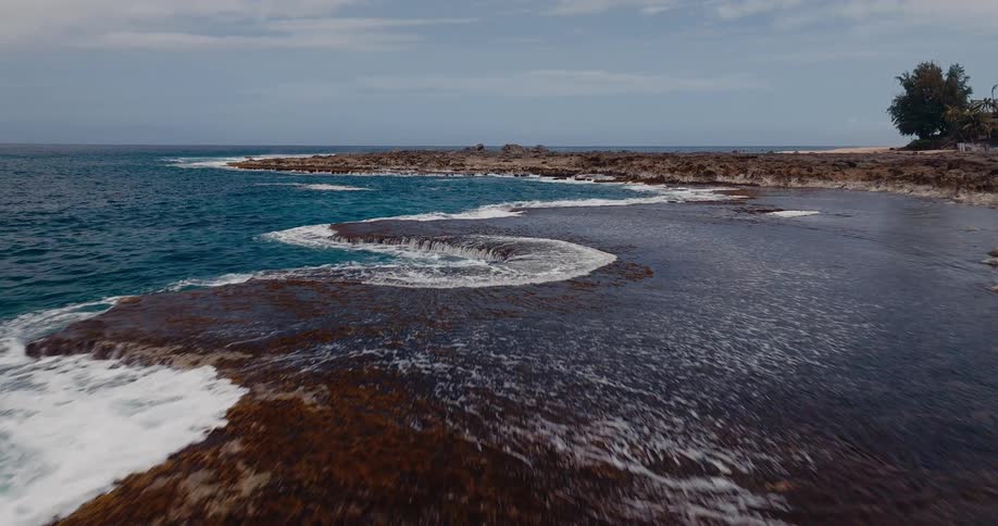 Aerial of ocean water waves flowing against coastal land formations during daytime