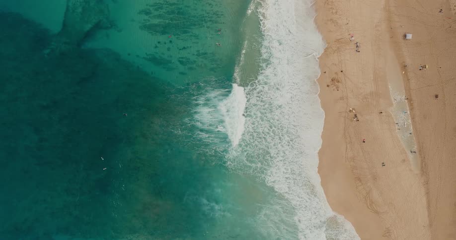 Waves breaking on the light sand along the beach seen from above
