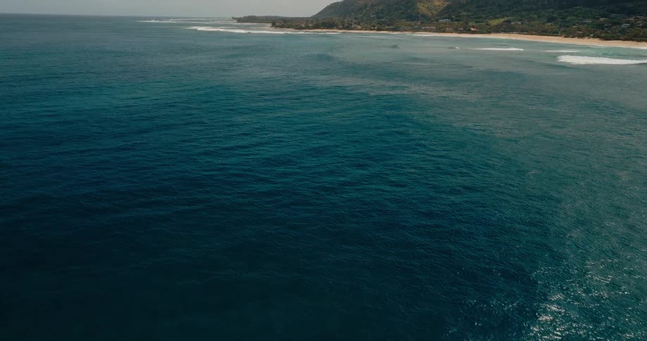 A mountainous coastline at midday with waves crashing against the shore