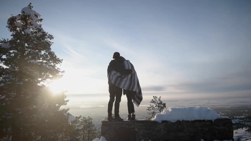 A man and woman hug while overlooking a snowy valley