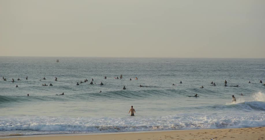 Person watches the sea while several surfers wait for waves