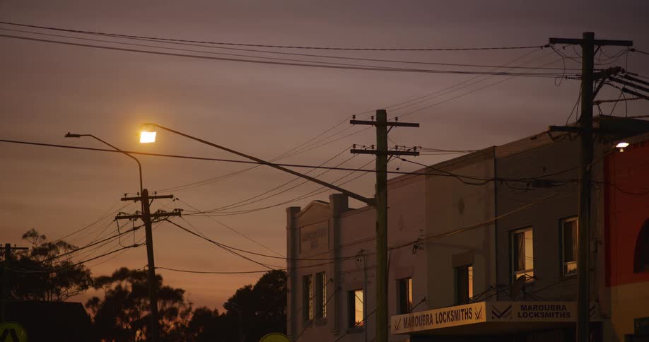 Utility poles and electrical wires lit by urban light at dusk