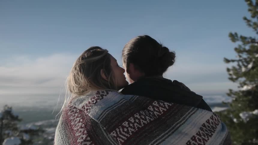 A man and woman share a blanket in the snowy mountains