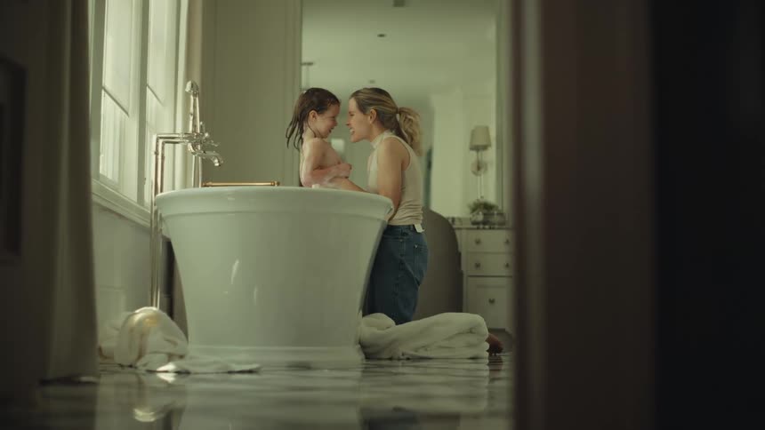 Mother touching her face to her daughters while the child sits in the bathtub