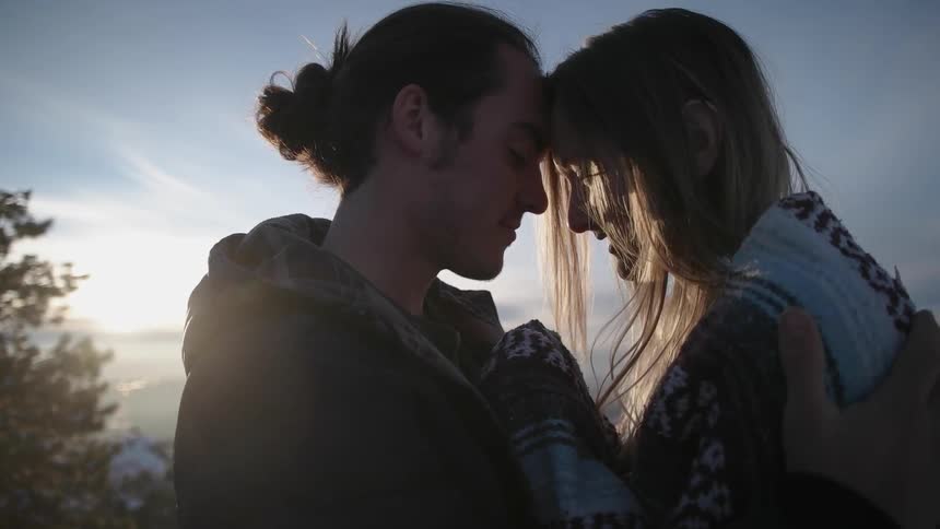 A man and woman cuddle with the sun shining behind them