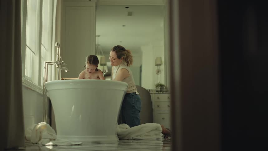 Mother playfully bathing daughter in a bathtub indoors during daytime