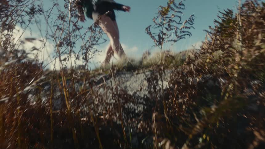 Female hiker walks across the grass near a slope on a cloudy autumn day