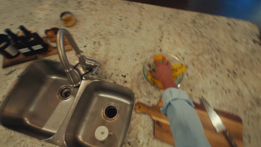 A person walks into the kitchen and grabs a fruit from the countertop