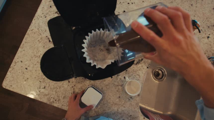 Ground coffee being poured into a coffee maker filter on a countertop