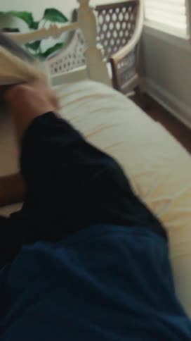 The legs and bare feet of a man are visible as he quickly sits up from a bright white bed and stretches in the sunlit bedroom