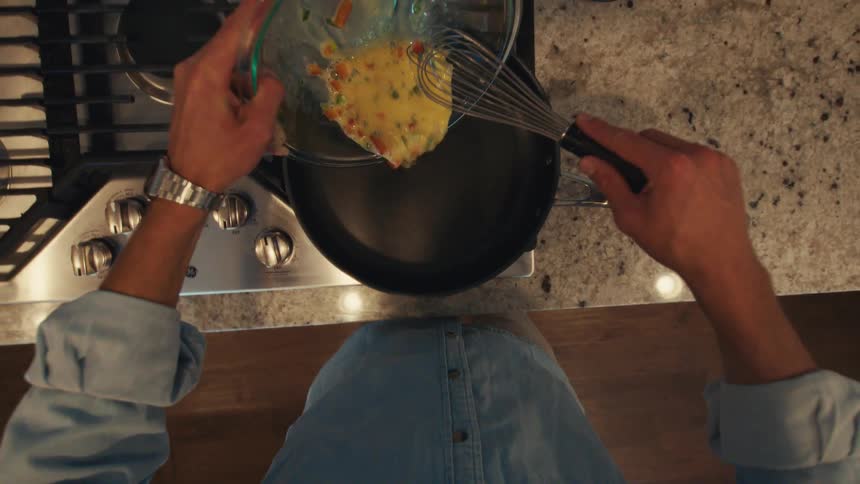 Man preparing eggs in his kitchen washes the bowl after pouring the egg mixture into a skillet on the stove