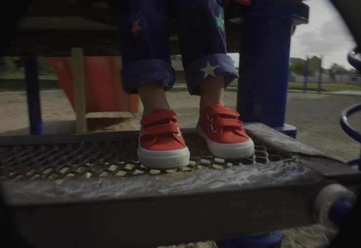 Child on a playground stepping down from a structure beside a spiral bar with lens flare in the frame
