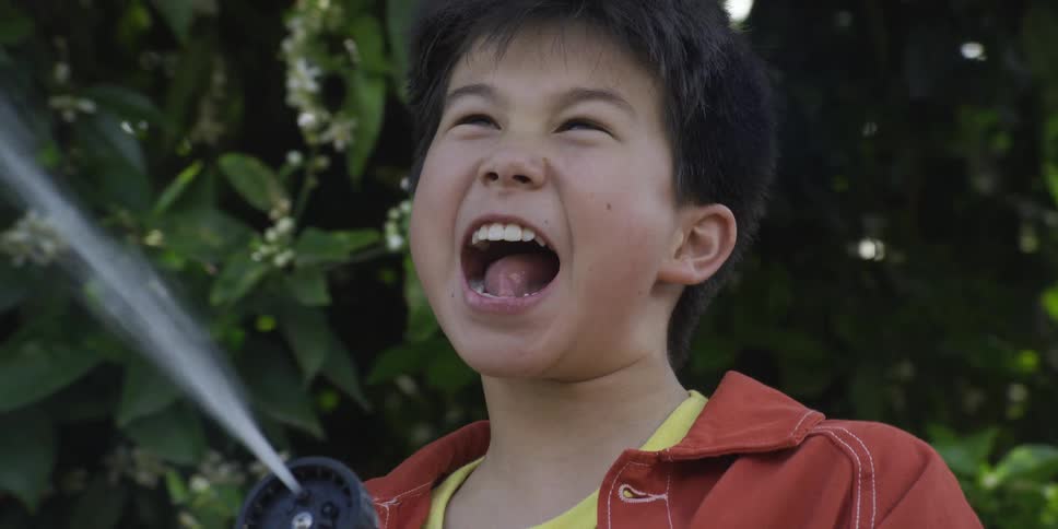 Boy holding a hose as a stream of water sprays beside his face