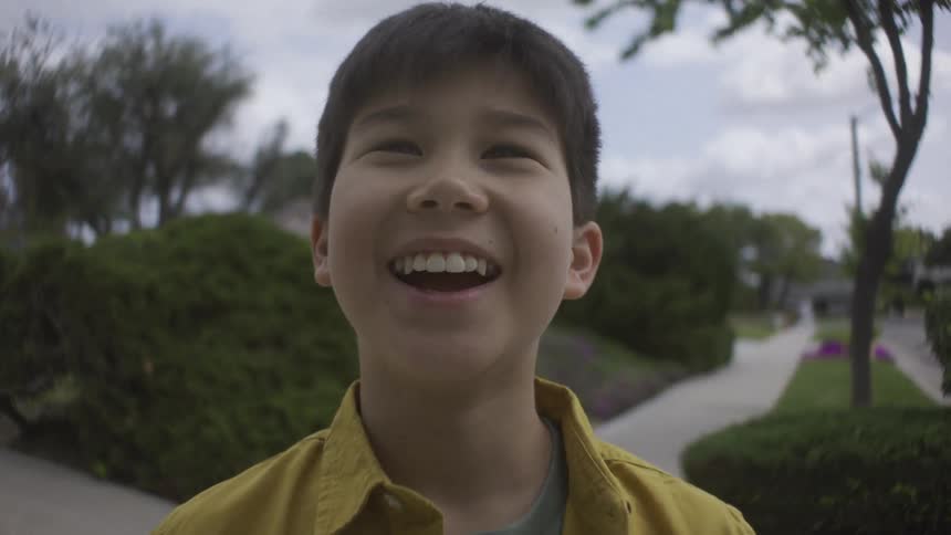 Young boy standing on a neighborhood sidewalk takes a deep breath with a smile on his face