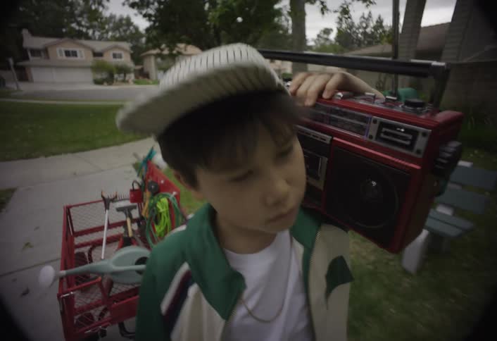 Boy walking with a portable radio resting on his shoulder in a residential neighborhood