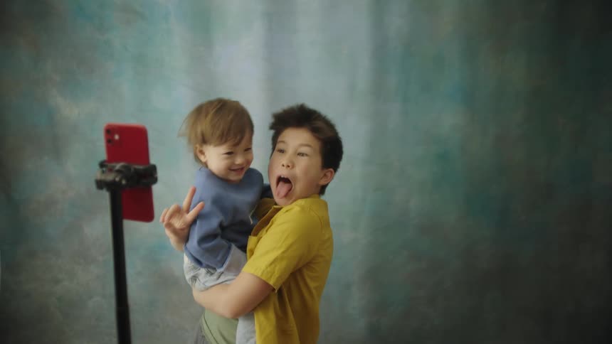 Two boys take a selfie making silly faces against a blue green backdrop