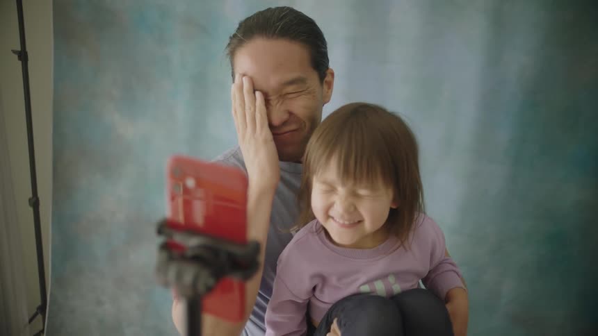 Man holds his young daughter as he takes a selfie picture with his phone