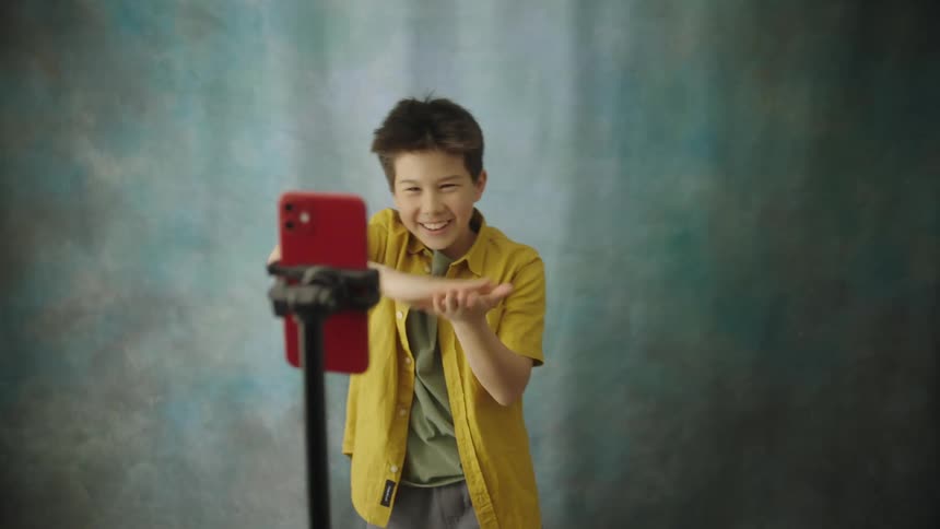 Boy making a gesture in front of a smartphone on a tripod during recording