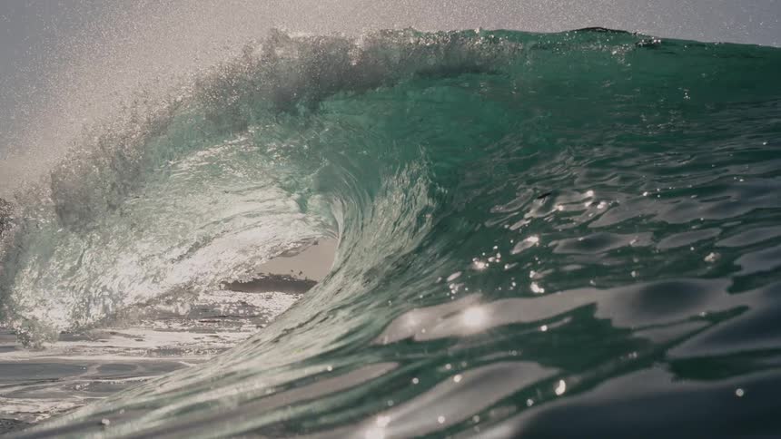 A towering ocean wave crests dramatically beneath a bright cloudy sky