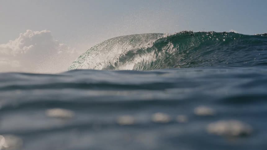This video captures a slowmotion closeup view of a deep blue ocean wave as it crests and begins to break sunlight reflects brilliantly off the waters surface just before the camera is submerged as the wave crashes