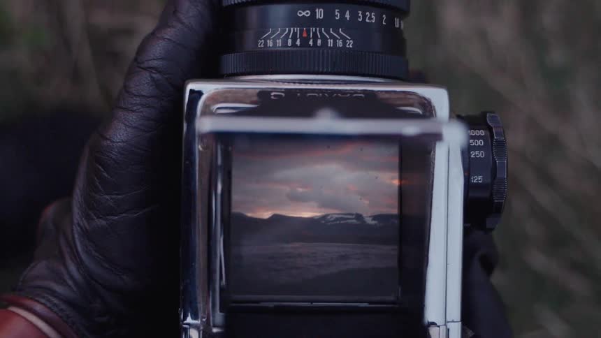 Closeup hands hold a medium format camera capturing a snow capped mountain at dusk