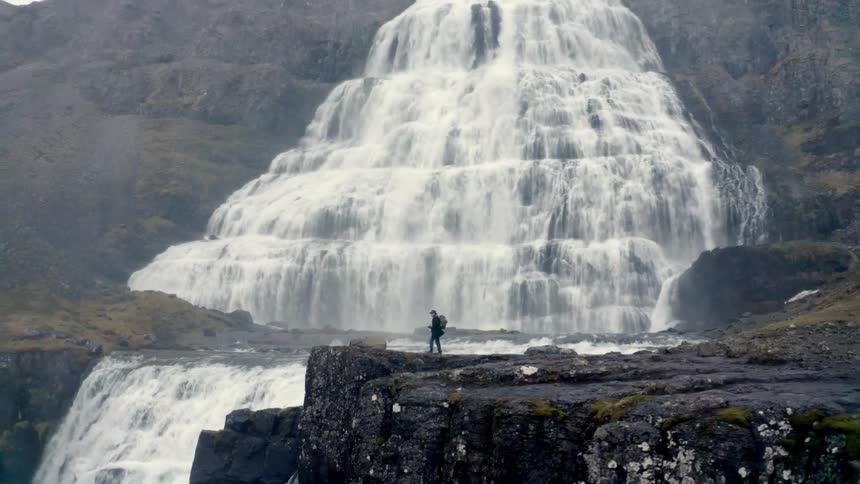 Person on a cliff observing a large tiered waterfall