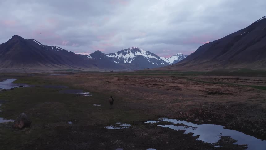 Wet plain surrounded by snowy mountains under a cloudy sky