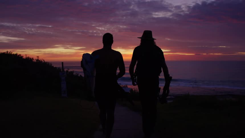 Two people walking toward the sea during a colorful sunset