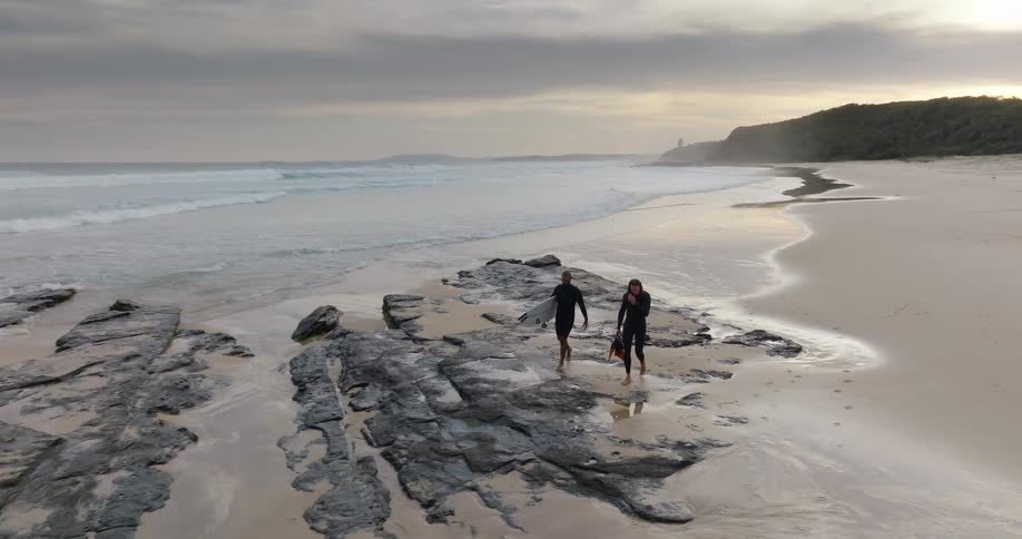 Two surfers walk on the beach