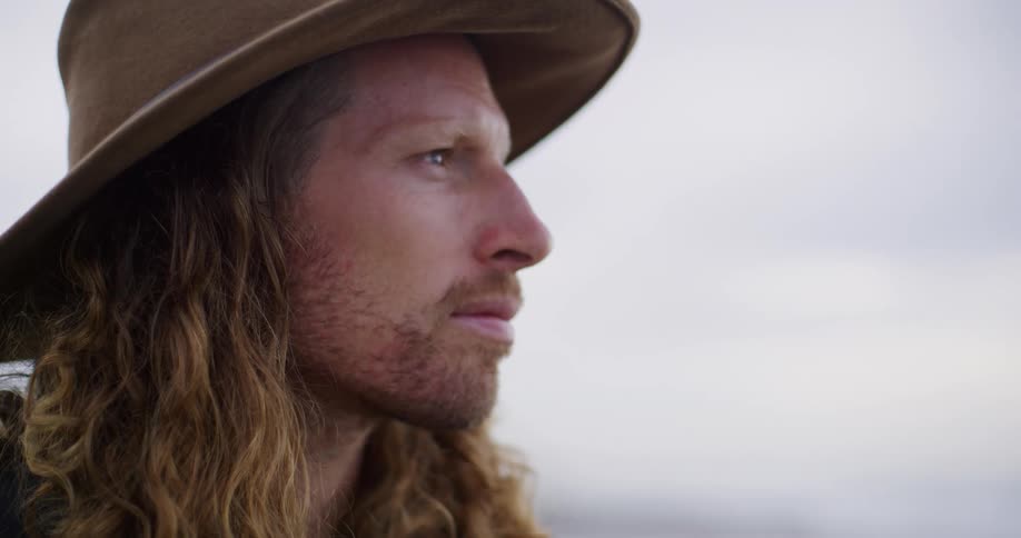 Closeup of a man with long hair wearing a hat gazing thoughtfully into the distance